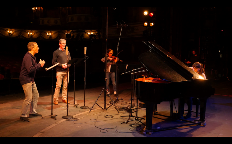 Vier mensen op een podium die muziekinstrumenten bespelen en zingen.