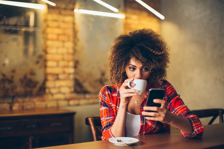 Een vrouw die een kop koffie drinkt, kijkt op haar smartphone.