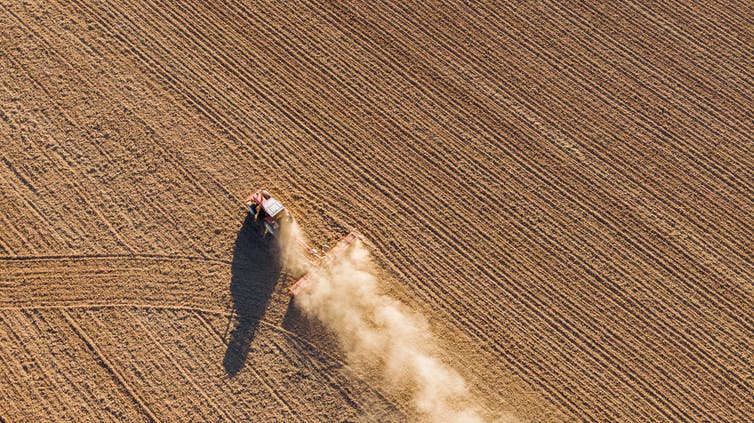 Een luchtfoto van een tractor die land bewerkt.