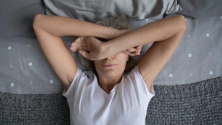 Vrouw ligt in bed met armen over haar gezicht