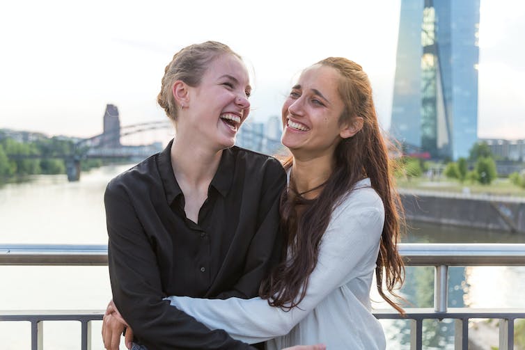 Twee jonge vrouwen staan op een brug en lachen samen.