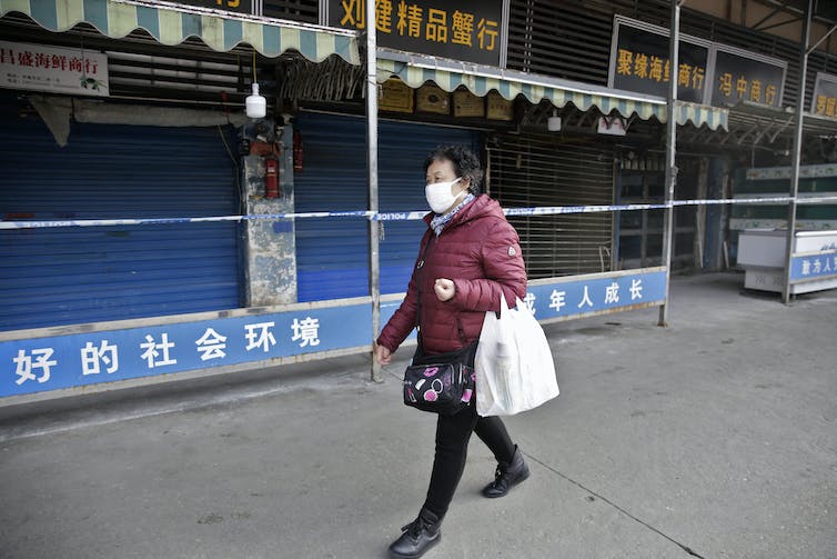 Een vrouw met een masker loopt langs de gesloten Huanan Seafood Wholesale Market in 2020.