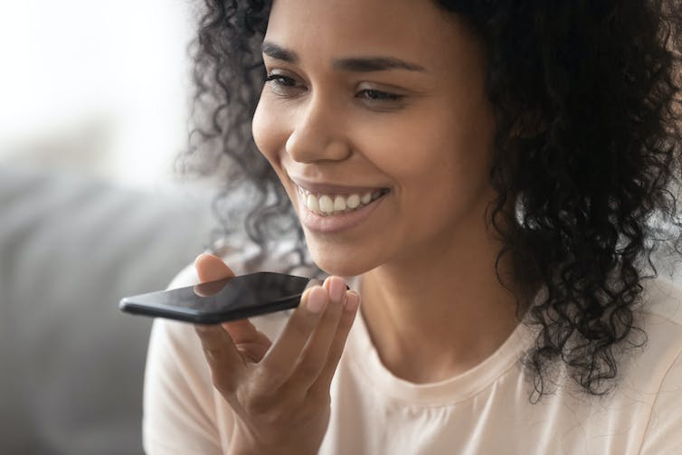 Een lachende vrouw houdt haar smartphone tegen haar mond om met een digitale assistent te spreken