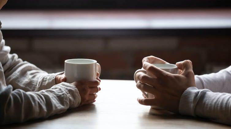 Close up vrouw en man zitten in café met warme kopjes koffie op tafel