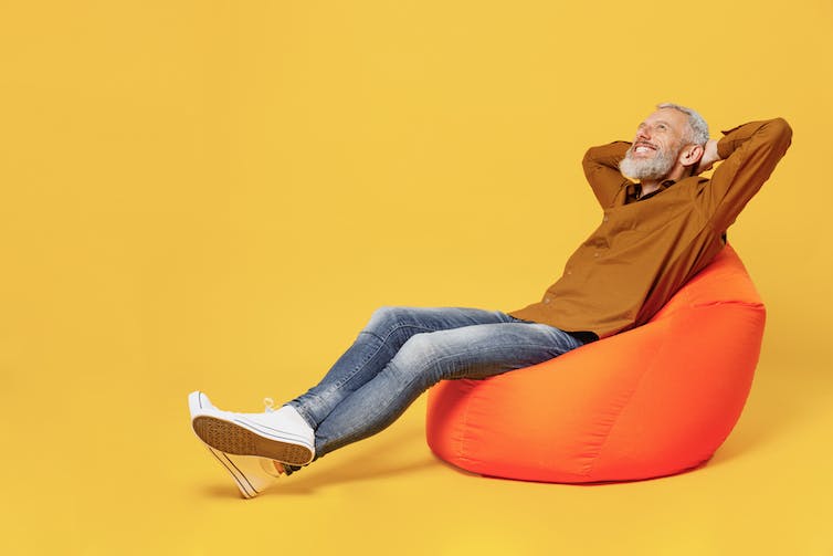 Een man zit op een oranje zitzak en doet de katapult lichaamstaal positie.