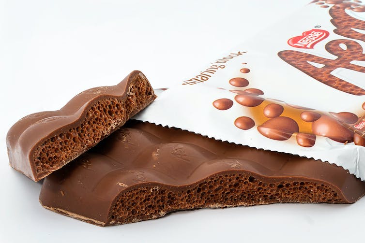 Een macro close-up opname van een geopende reep Aero chocolade, met de hoek afgebroken, waardoor de unieke bubbelstructuur waaraan hij zijn naam dankt, zichtbaar wordt.