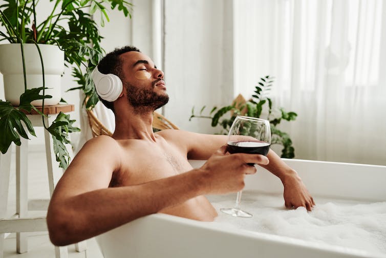 Man ontspant in bad met glas wijn omringd door kamerplanten