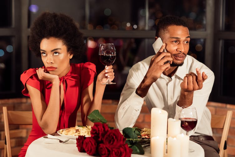 Man pratend op zijn telefoon zat naast een vrouw met een glas wijn die geërgerd keek.