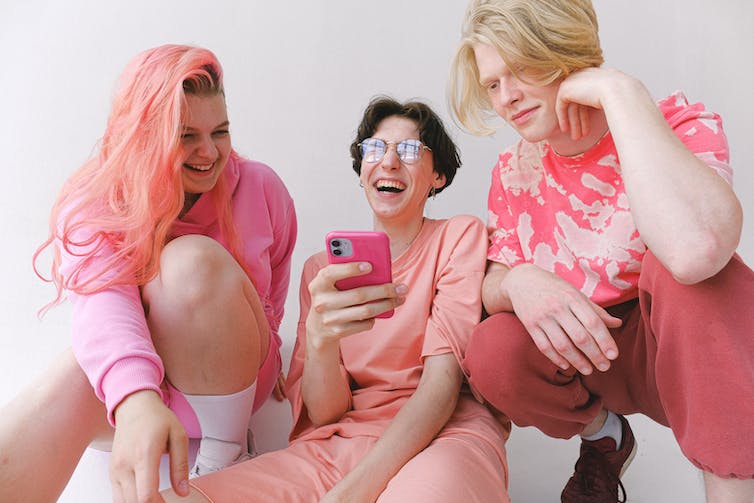 Groep vrienden, in het roze, kijkend naar een telefoon.
