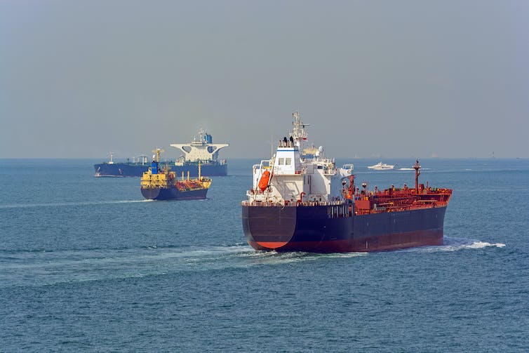 Drie industriële schepen passeren elkaar op de oceaan.