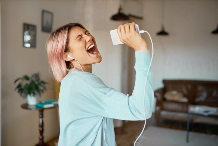 Vrouw met roze haar zingt in muziekapparaat met koptelefoon op.