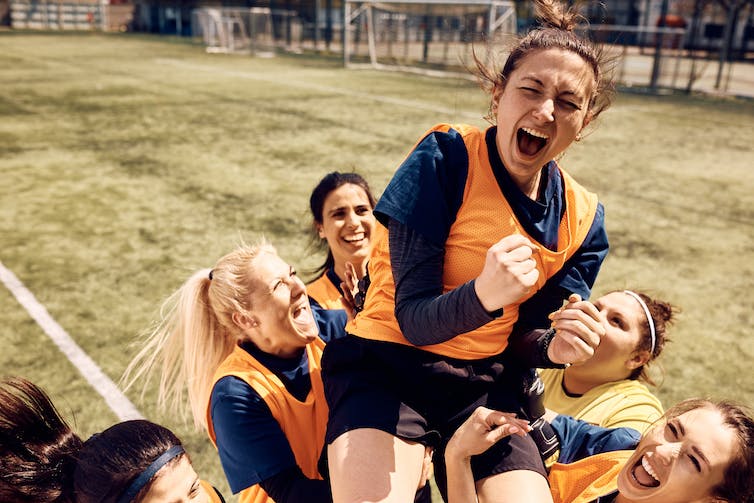 Vrolijk team van vrouwelijke voetballers viert overwinning en draagt teamgenoten die schreeuwen van vreugde