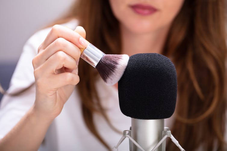 Vrouw borstelt een microfoon met een make-upborstel.