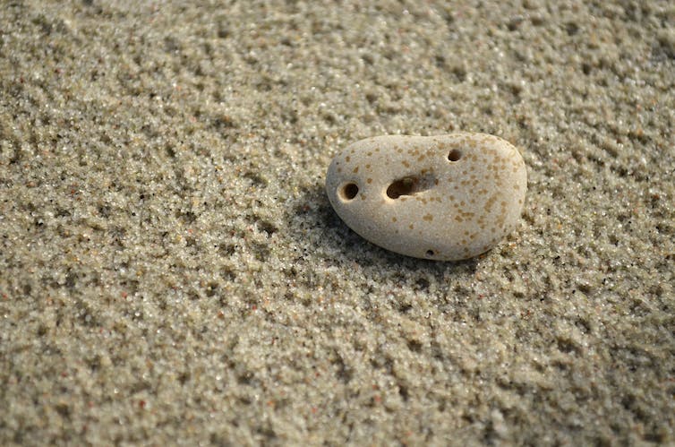 Kiezel op zand, inkepingen in de rots lijken een gezicht te vormen