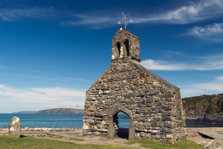 Een stenen muur van een kerk staat aan een prachtige kustlijn.