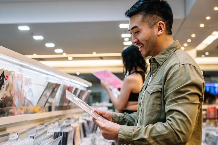 Een jongeman glimlacht terwijl hij in een winkel door een selectie vinylplaten bladert