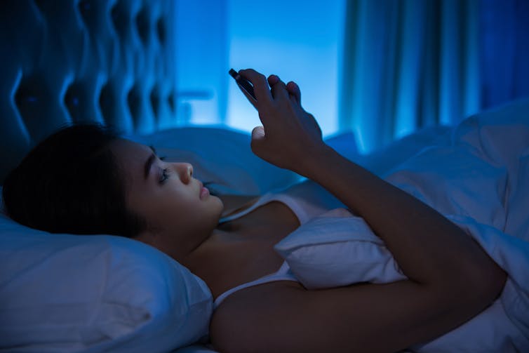 Jonge Aziatische vrouw ligt in bed verlicht door de gloed van haar telefoon
